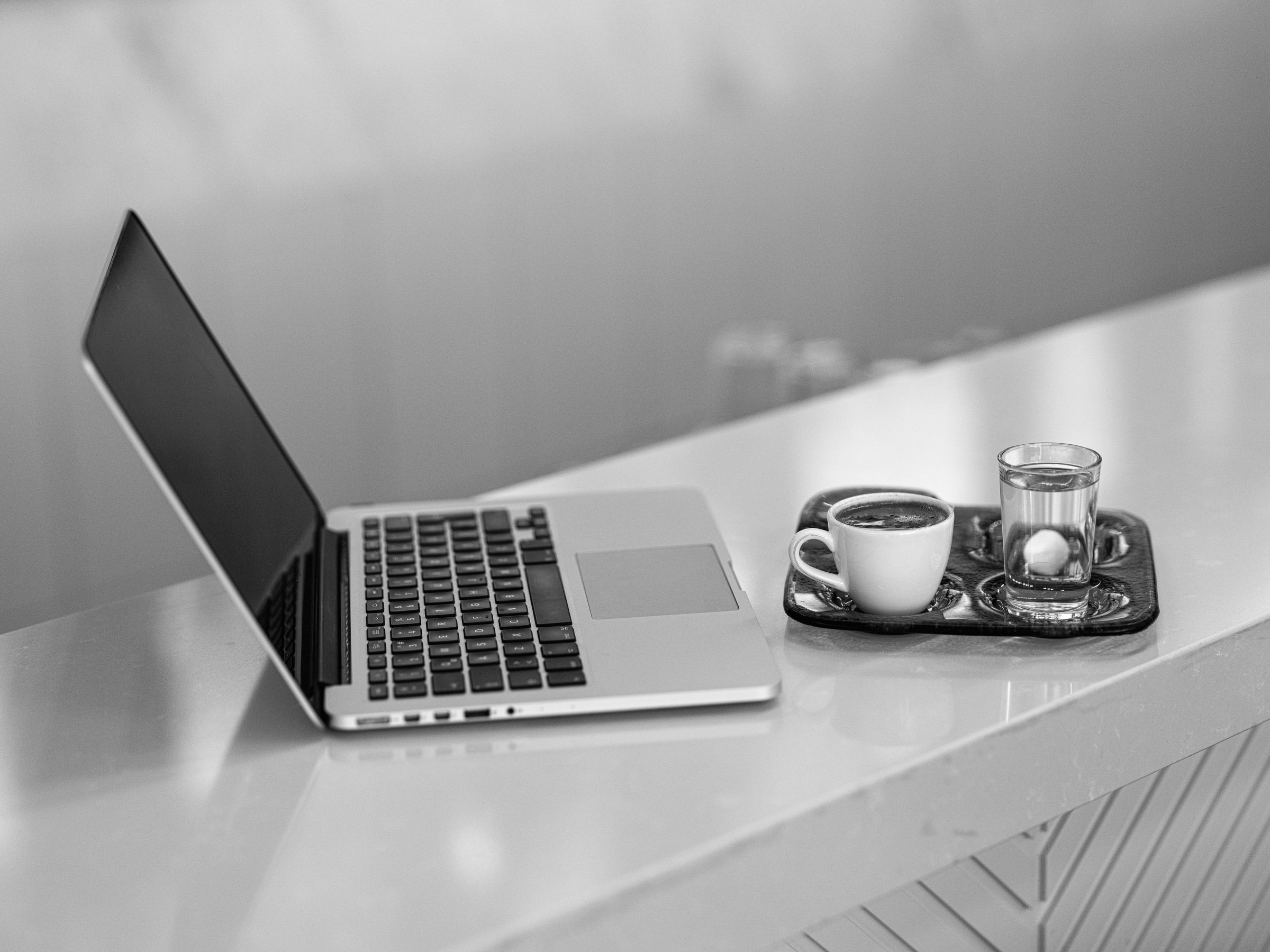 Laptop on a white bench beside a coffee and a glass of water